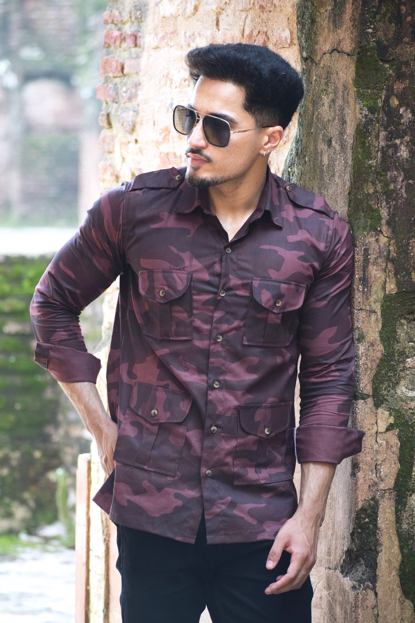 Man wearing a maroon camouflage shirt leaning against a tree