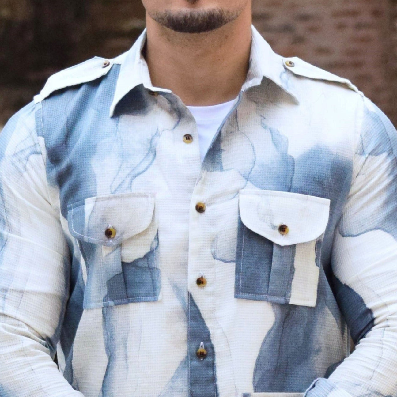 Man wearing a checkered shirt and sunglasses standing in front of a stone wall.