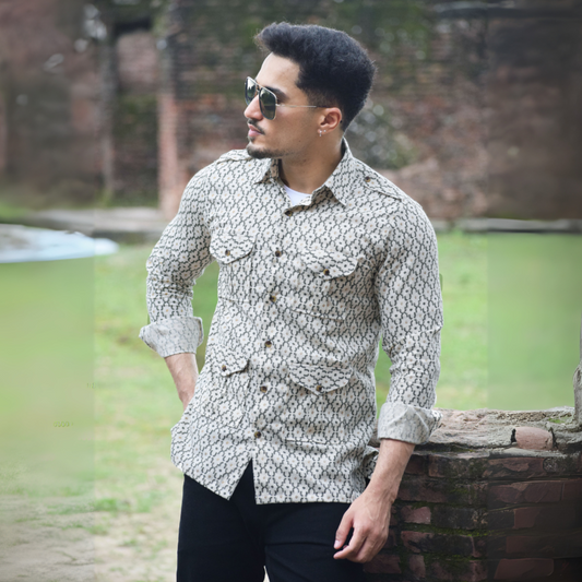 Man wearing a patterned shirt and sunglasses, standing outdoors near a body of water.