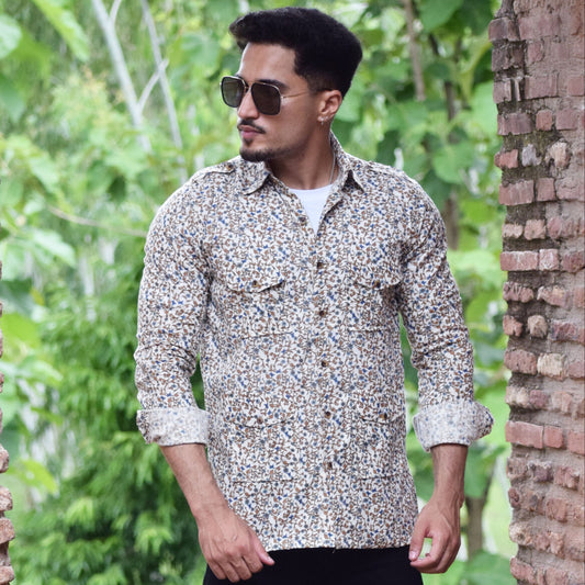 Man wearing a patterned shirt and sunglasses standing between two brick walls with greenery in the background