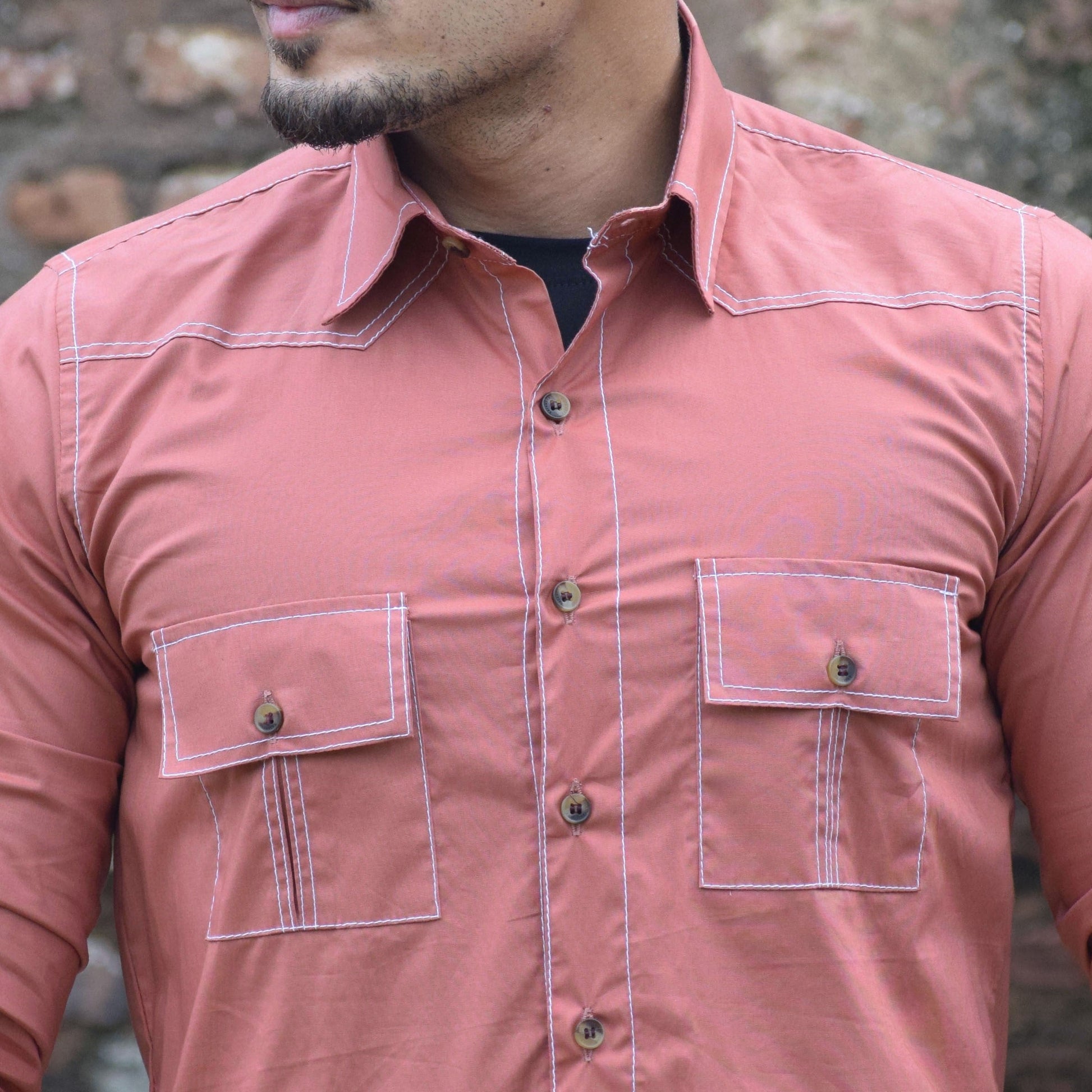Man wearing a pink shirt with multiple pockets against a brick wall.