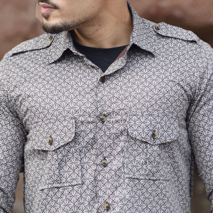 Man wearing a patterned shirt with rolled-up sleeves against a textured wall.