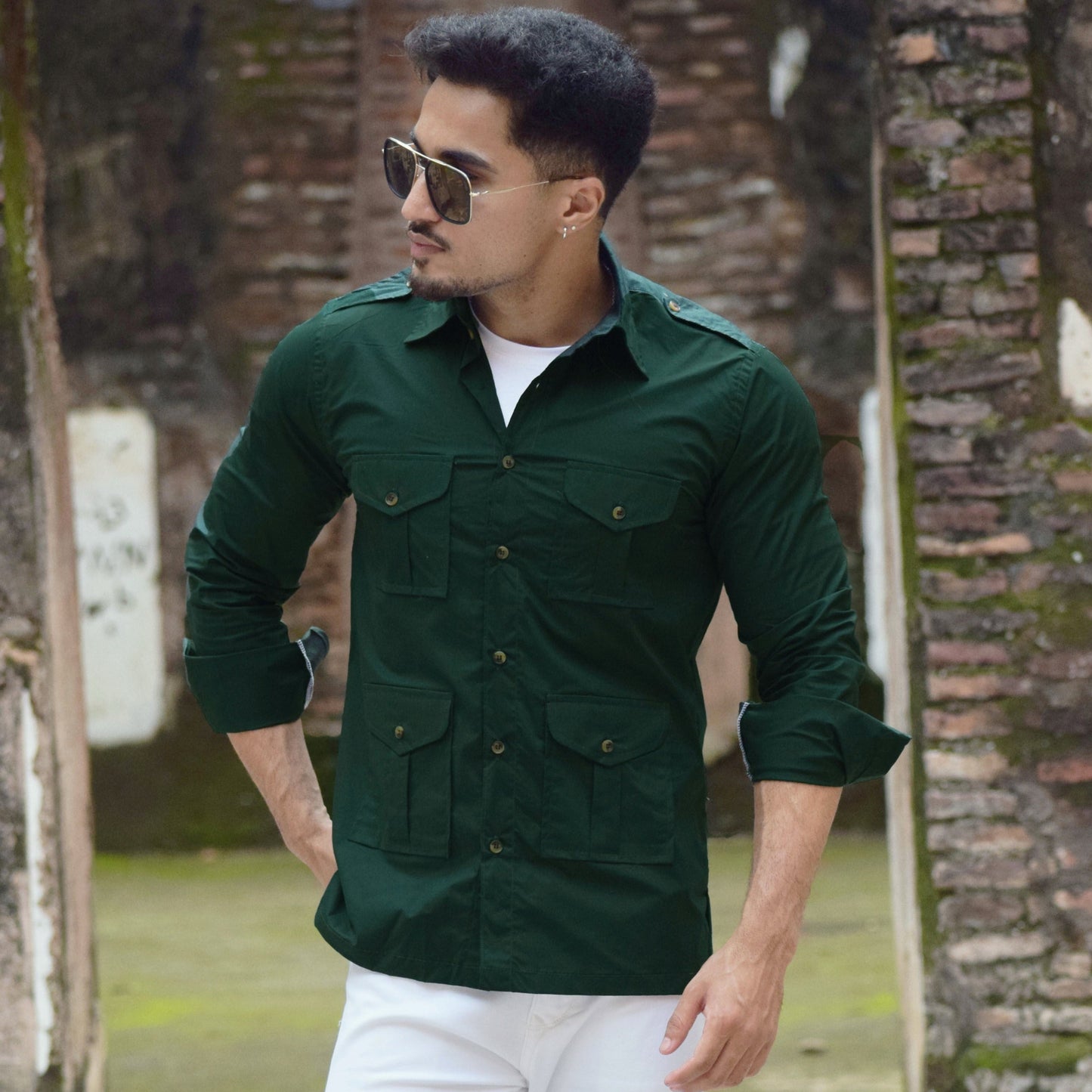 Man wearing a green shirt and white pants standing in front of a brick wall.