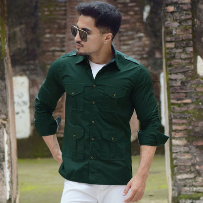 Man wearing a green shirt and white pants standing in front of a brick wall.