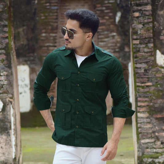 Man wearing a green shirt and white pants standing in front of a brick wall.
