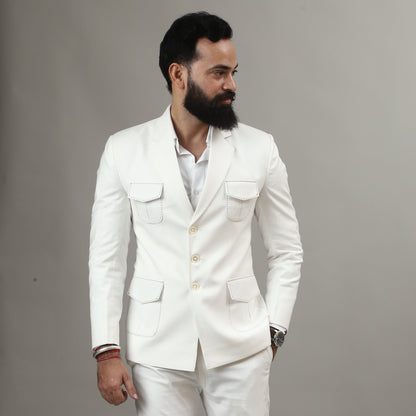 Man wearing a white suit standing next to a wooden stool on a plain background