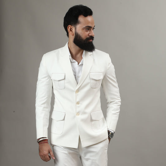 Man wearing a white suit standing next to a wooden stool on a plain background