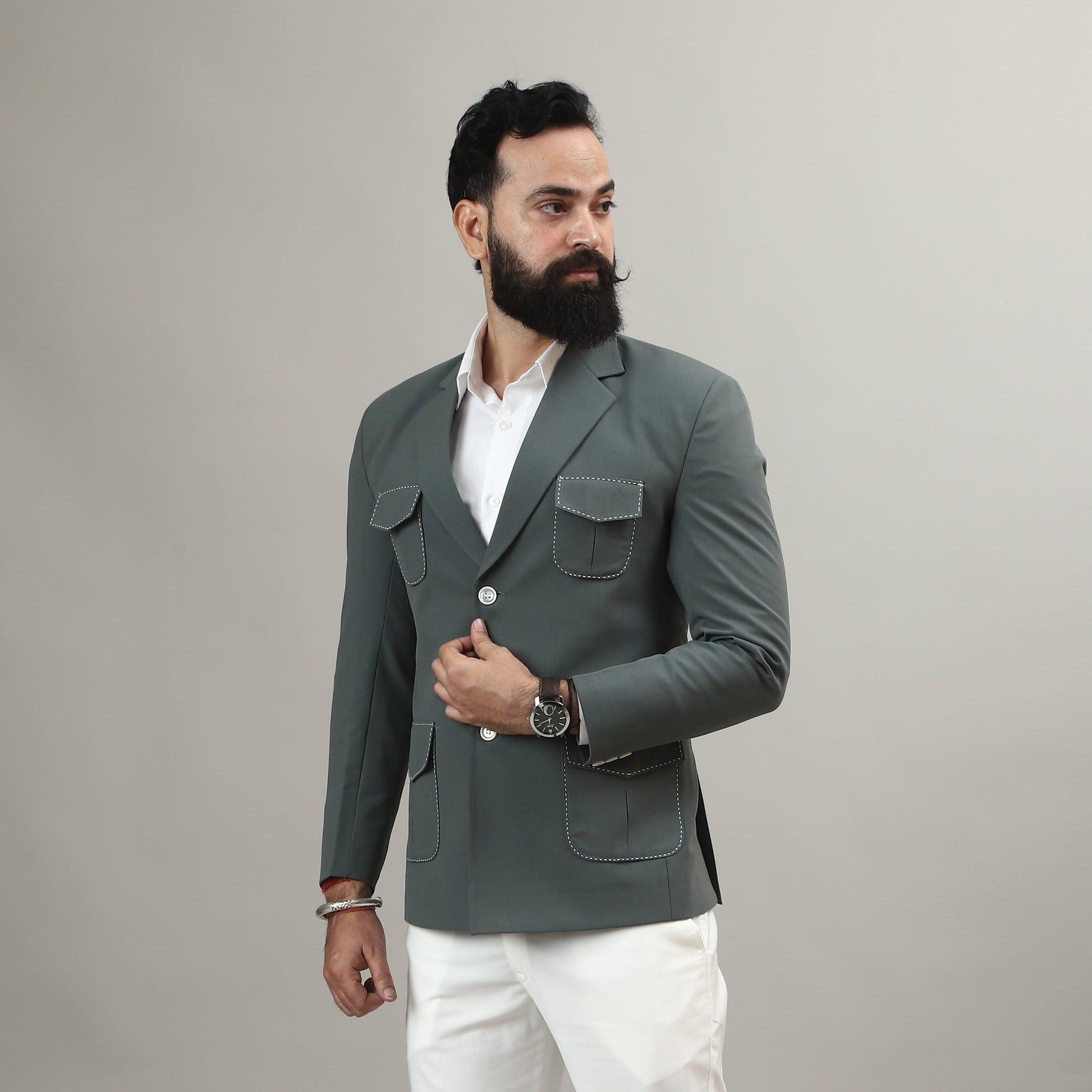 Man wearing a gray blazer, white shirt, and white pants against a plain background