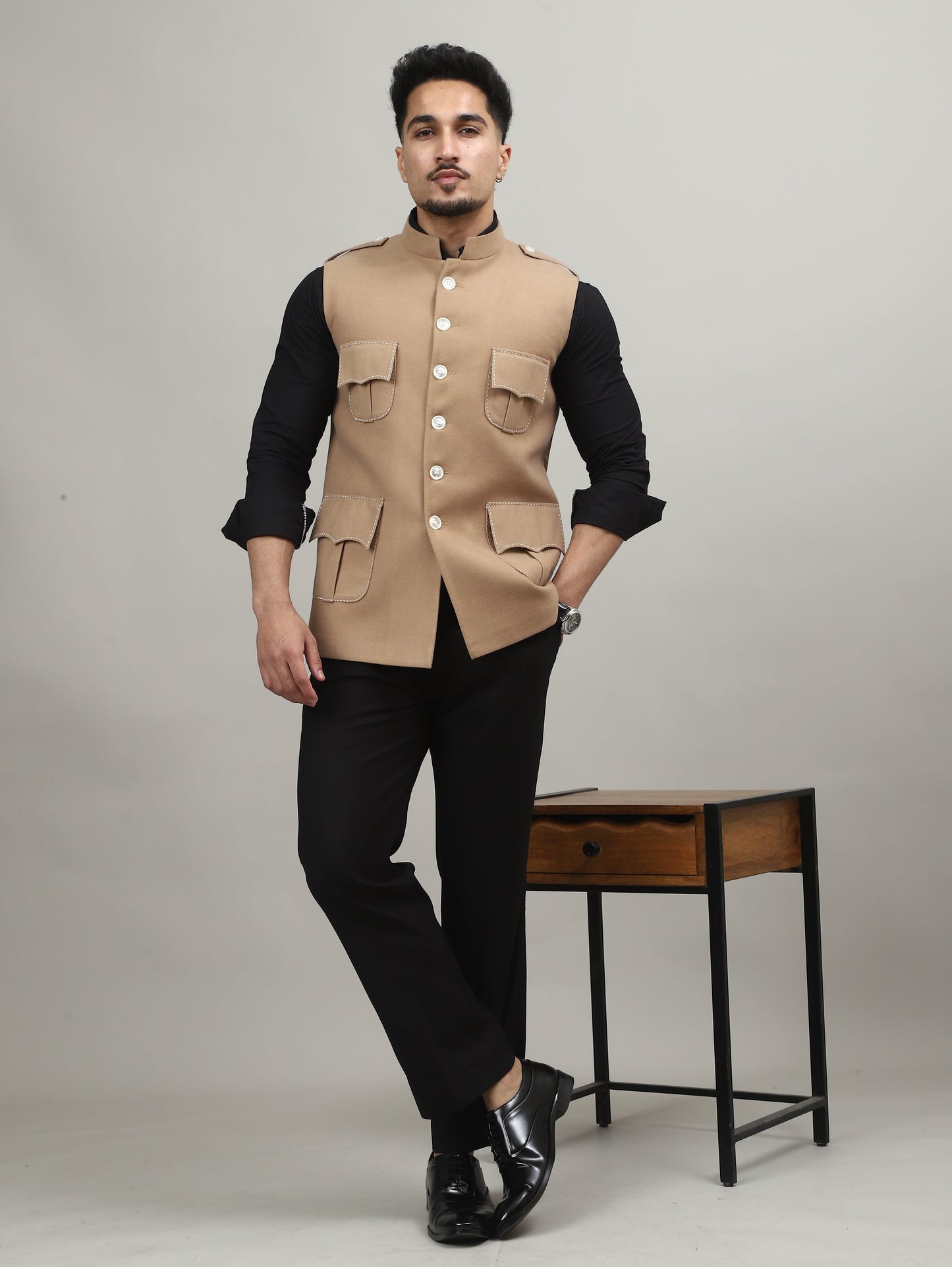 Person wearing a beige vest over a black long-sleeve shirt on a white background