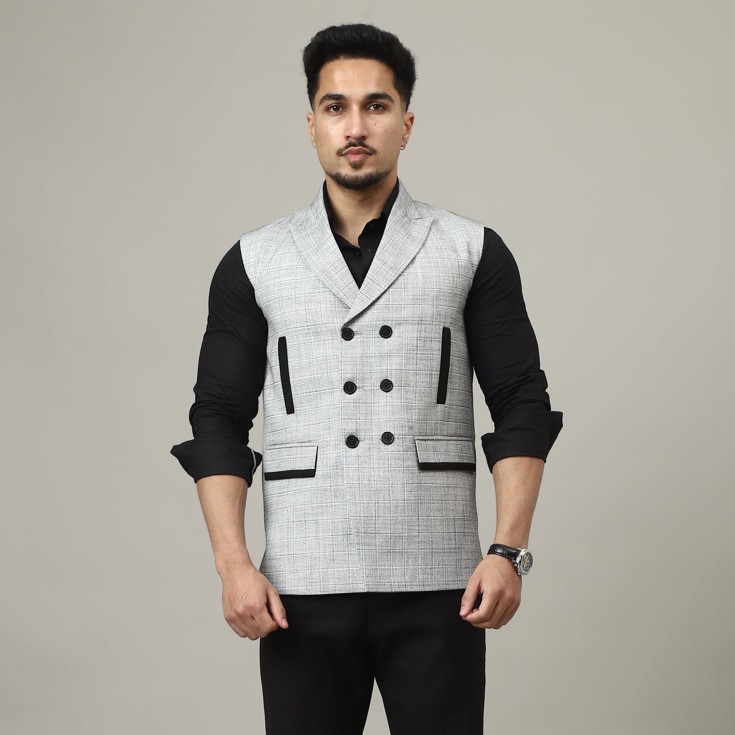 Man wearing a black and white patterned vest over a black shirt and black pants on a plain background