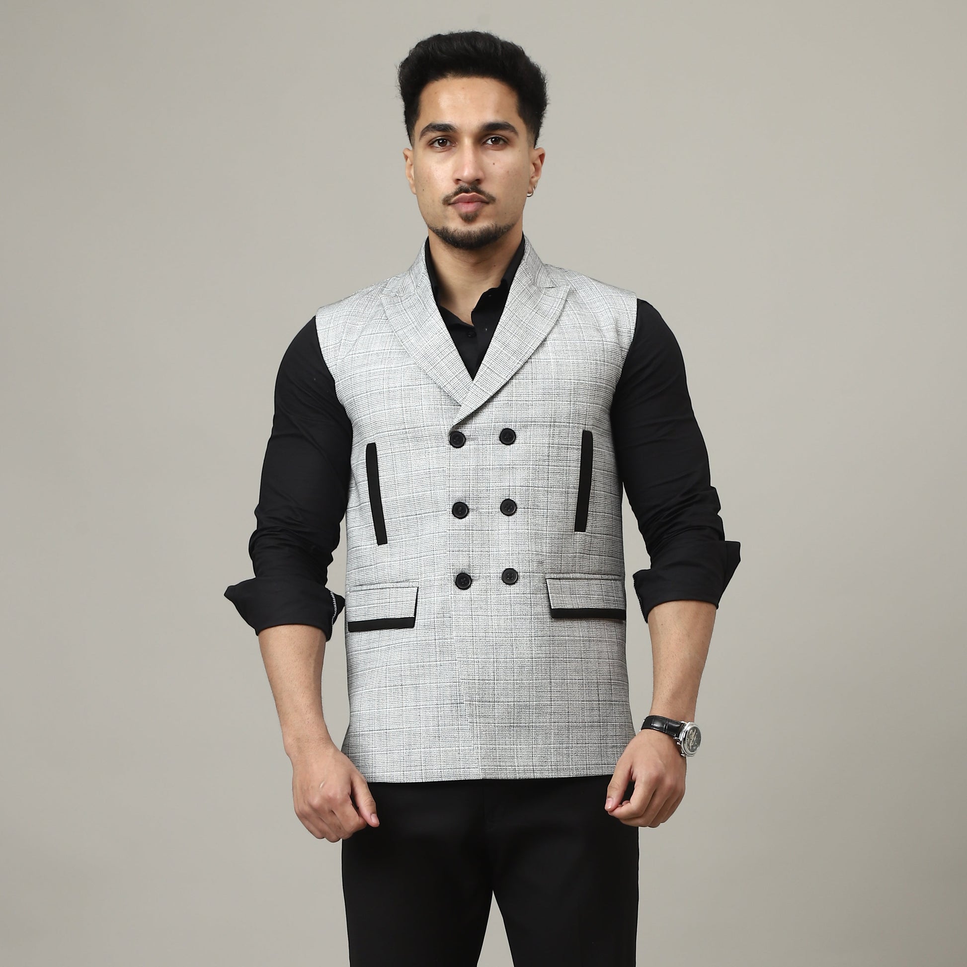 Man wearing a black and white patterned vest over a black shirt and black pants on a plain background