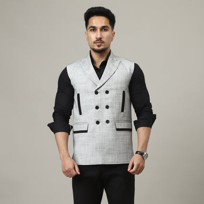 Man wearing a black and white patterned vest over a black shirt and black pants on a plain background