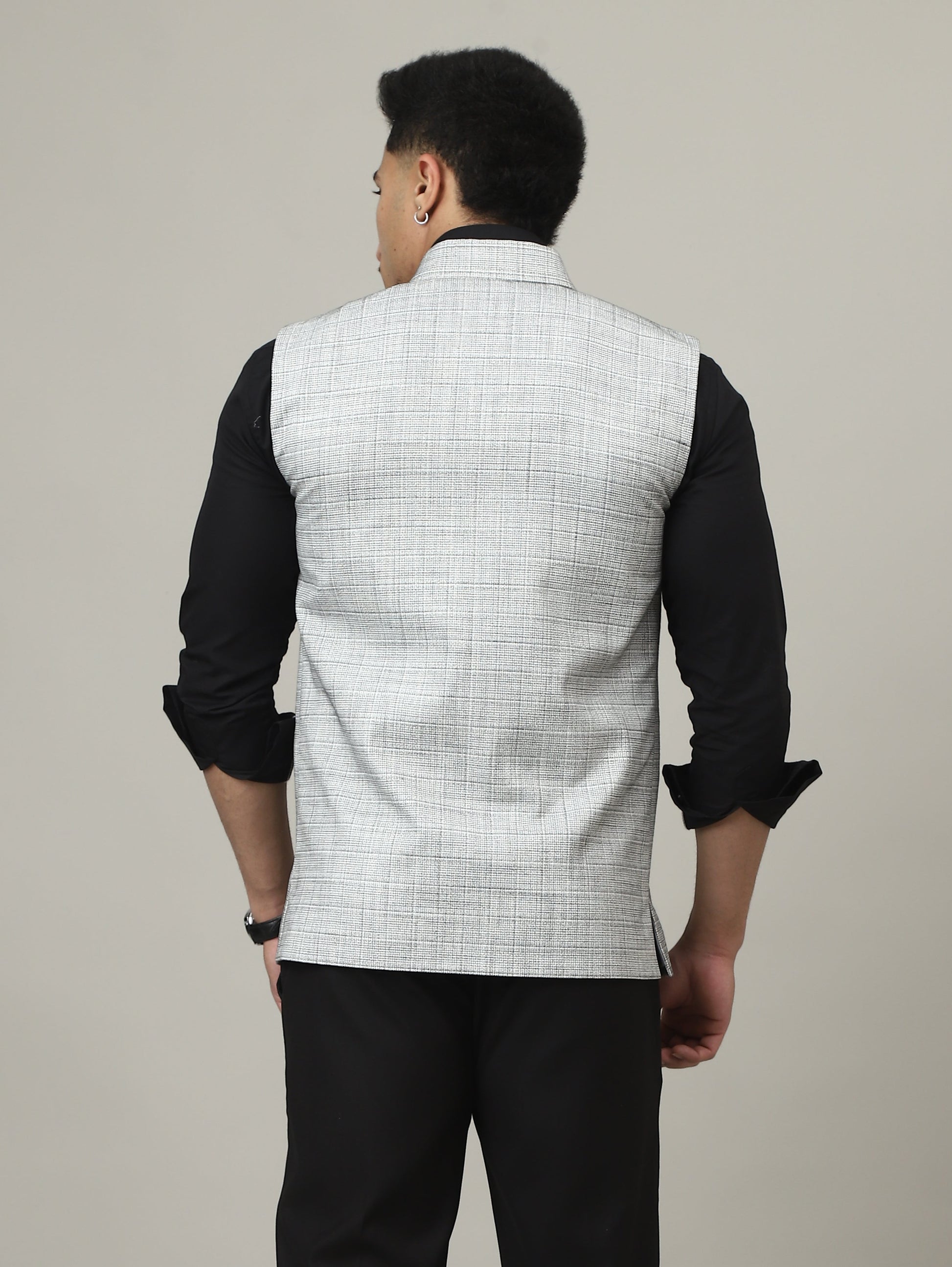 Person wearing a black outfit with a white vest against a plain background