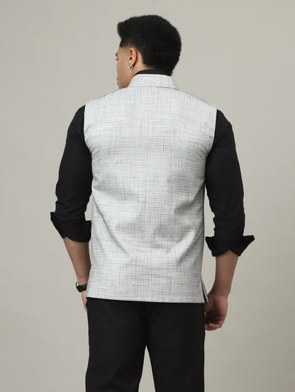 Person wearing a black outfit with a white vest against a plain background