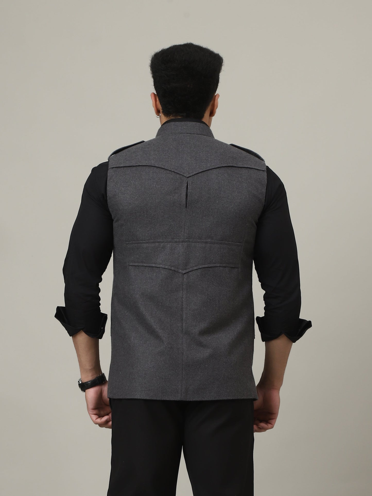 Person wearing a gray blazer over a black shirt with black pants and shoes on a plain background