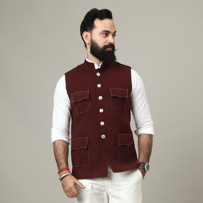 Man wearing a maroon vest over a white shirt against a plain background