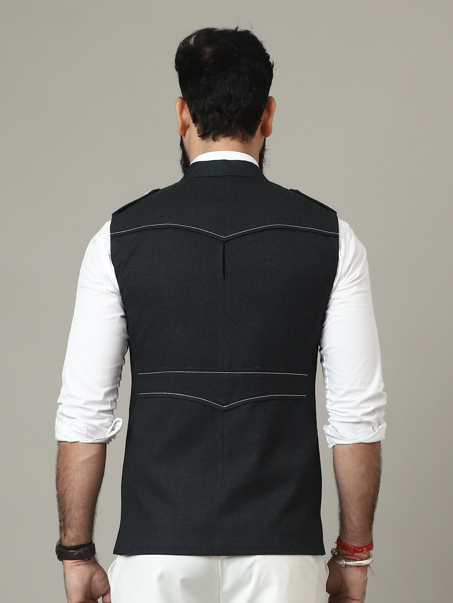 Person wearing a black vest over a white shirt with white pants on a plain background