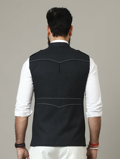 Person wearing a black vest over a white shirt with white pants on a plain background