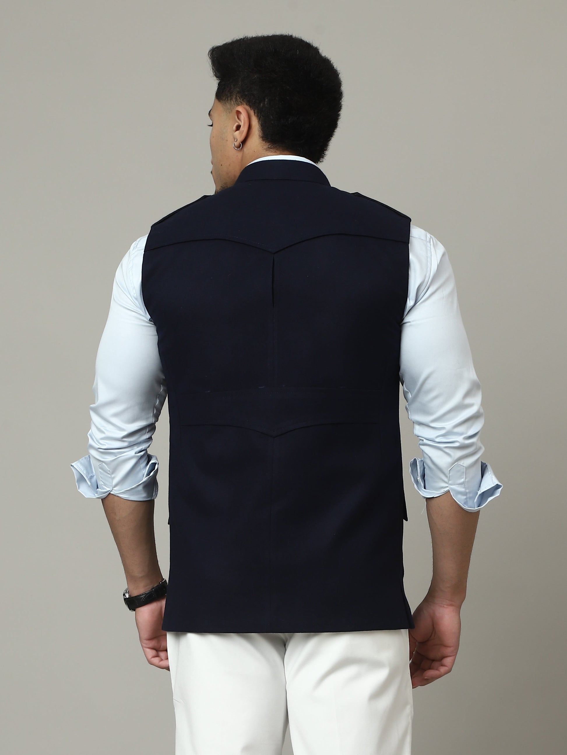 Person wearing a white shirt, black vest, and white pants against a plain background