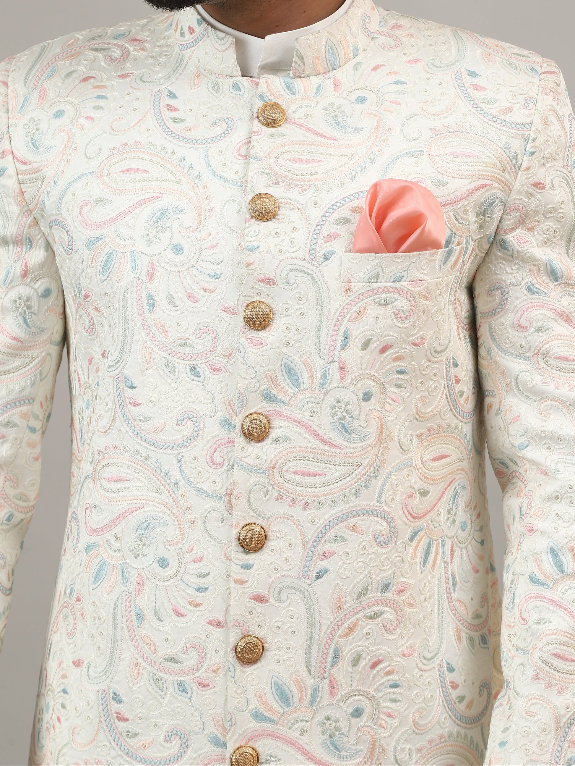 Man wearing a traditional embroidered sherwani against a plain background