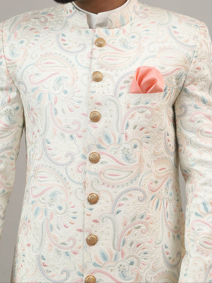 Man wearing a traditional embroidered sherwani against a plain background
