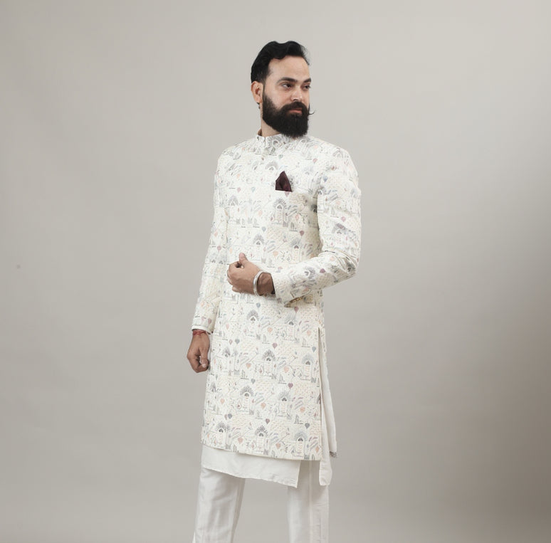 Person wearing a Rajanyas white Sherwani outfit with a floral pattern on a plain background