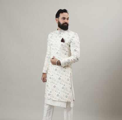 Person wearing a Rajanyas white Sherwani outfit with a floral pattern on a plain background