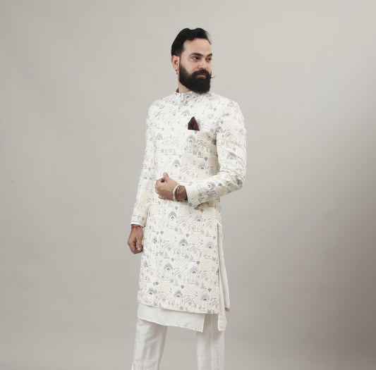 Person wearing a Rajanyas white Sherwani outfit with a floral pattern on a plain background