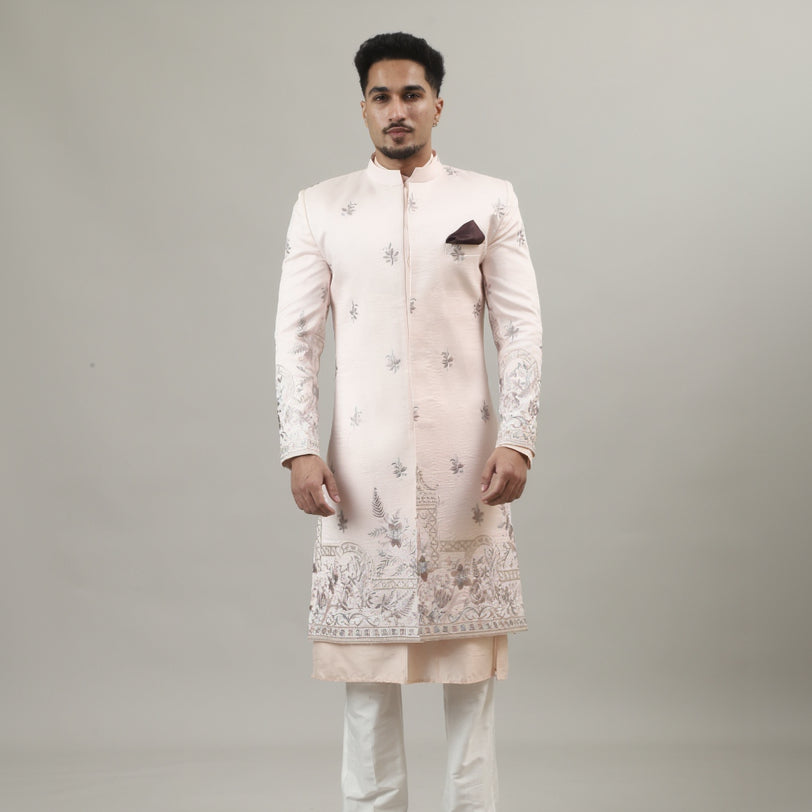 Person wearing a traditional embroidered sherwani on a plain background