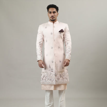 Person wearing a traditional embroidered sherwani on a plain background
