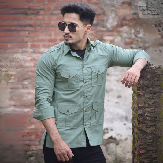 Man wearing a light green shirt and sunglasses leaning against a textured wall.
