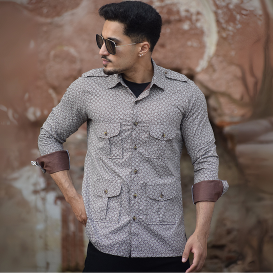 Man wearing a patterned shirt with rolled-up sleeves in front of a textured wall.