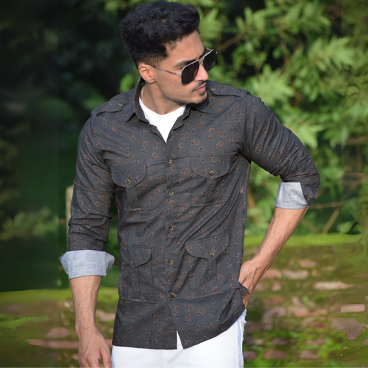 Man wearing sunglasses and a patterned shirt outdoors with greenery in the background