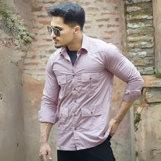 Man wearing a light pink shirt and sunglasses against a rustic wall.