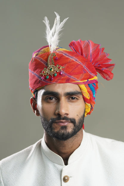 A man wearing a traditional Safa turban in purple, multicolored patterns with decorative elements on the top.
